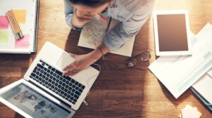 Young female entrepreneur thinking and browsing laptop in office