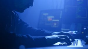 Close-up of professional computer hacker writing data codes typing on laptop at night in the office.